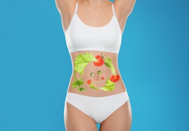 Slim young woman and images of vegetables on her belly against light blue background. Healthy eating