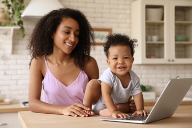 African-American woman and her baby with laptop in kitchen. Happiness of motherhood
