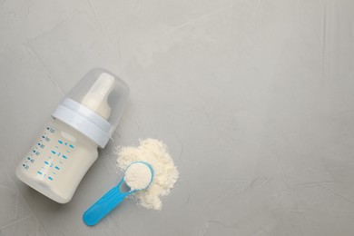 Feeding bottle with infant formula, scoop of powder and space for text on grey table, flat lay. Baby milk