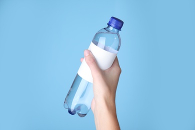 Woman holding plastic bottle with soda water on light blue background, closeup
