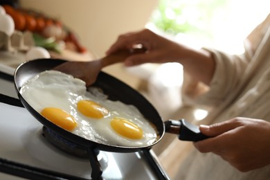 Woman cooking tasty eggs on frying pan in kitchen, closeup