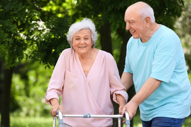 Elderly man helping his wife with walking frame outdoors