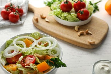Photo of Bowl of delicious salad with Chinese cabbage, tomatoes and onion on white wooden table, closeup