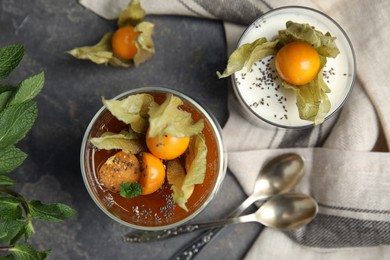 Delicious desserts decorated with physalis on grey table, flat lay