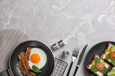 Tasty breakfast with fried egg, bacon and sandwiches served on light grey marble table, flat lay. Space for text