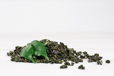 Heap of dried green tea leaves on white table