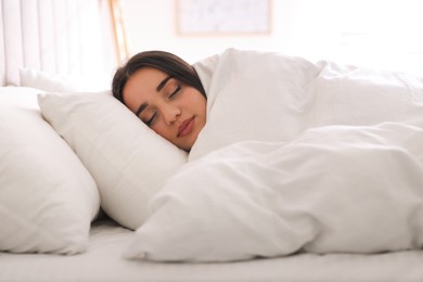 Young woman covered with warm white blanket sleeping in bed at home