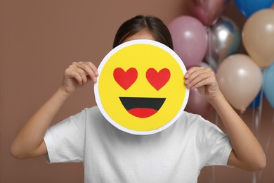 Little girl covering face with heart eyes emoji in decorated room
