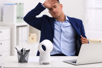 Man suffering from heat at workplace, focus on fan