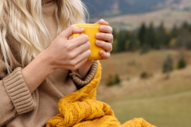 Young woman with mug of hot drink outdoors, closeup. Space for text