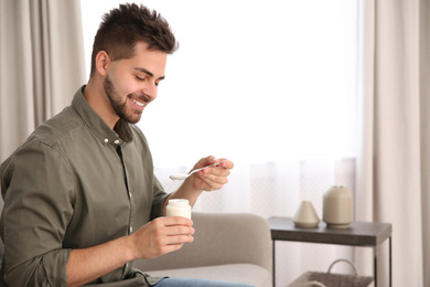 Happy young man with tasty yogurt in living room. Space for text