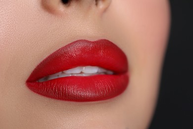 Young woman wearing beautiful red lipstick on black background, closeup