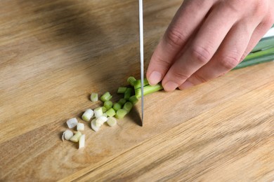 Woman cutting green spring onion on wooden board, closeup