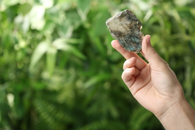 Woman holding beautiful labradorite gemstone on blurred green background, closeup. Space for text