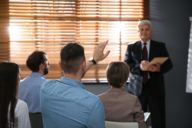 Man raising hand to ask question at seminar in office