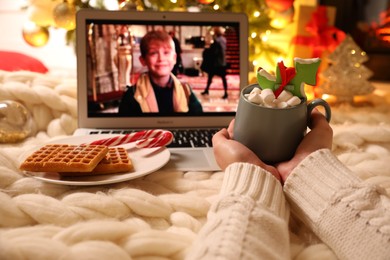 Photo of MYKOLAIV, UKRAINE - DECEMBER 23, 2020: Woman with sweet drink watching Home Alone movie on laptop at home, closeup. Cozy winter holidays atmosphere