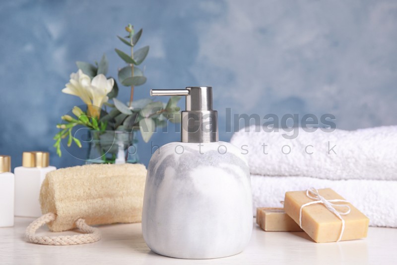 Marble dispenser, soap bars and luffa sponge on white wooden table