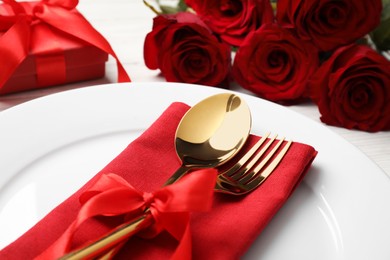 Photo of Beautiful dishware with gift and bouquet on white wooden table, closeup. Romantic date