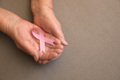 Senior woman holding pink ribbon on grey background, top view with space for text. Breast cancer awareness