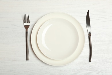 Empty dishware and cutlery on light wooden background, top view. Table setting
