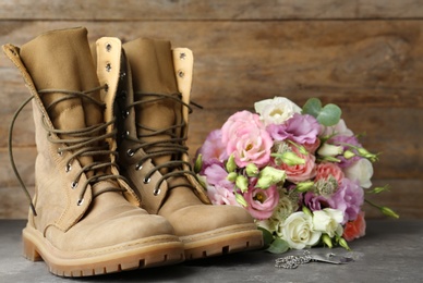 Military boots with flowers on grey stone surface, space for text. Armed Forces Day