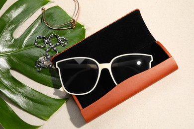 Flat lay composition with stylish sunglasses and brown leather case on sand