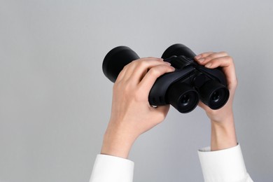 Photo of Woman holding modern binoculars on grey background, closeup. Space for text