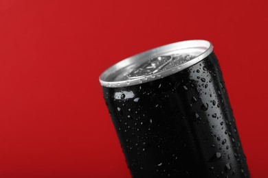 Black can of energy drink with water drops on red background, closeup. Space for text