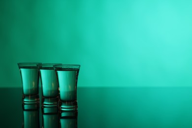 Vodka in shot glasses on green background, space for text