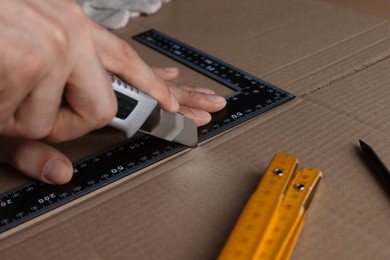 Man cutting cardboard with utility knife and ruler, closeup