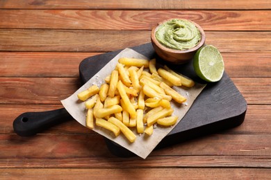 Serving board with french fries, avocado dip and lime served on wooden table