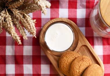 Photo of Glass of milk with cookies on red checkered tablecloth, flat lay