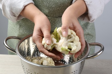 Woman separating fresh cauliflower cabbage above colander at wooden table, closeup