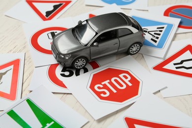 Cards with different road signs and toy car on white wooden table. Driving school