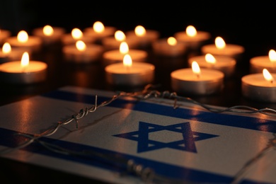Flag of Israel, barbed wire and burning candles on black background. Holocaust memory day