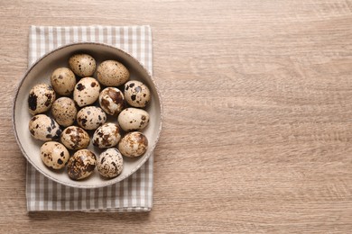 Bowl with quail eggs on wooden table, top view. Space for text