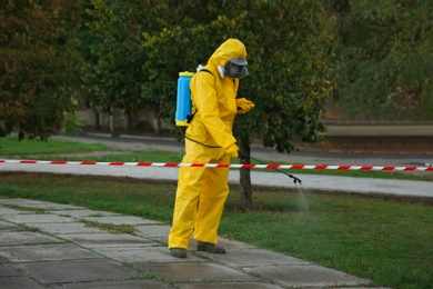Person in hazmat suit disinfecting street pavement with sprayer. Surface treatment during coronavirus pandemic