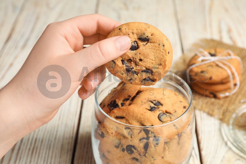 Woman taking chocolate chip cookie out of jar on white wooden table, closeup