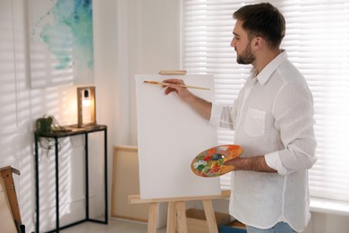 Young man painting on easel with brush in artist studio