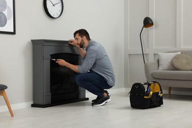 Man with screwdriver installing electric fireplace near wall in room