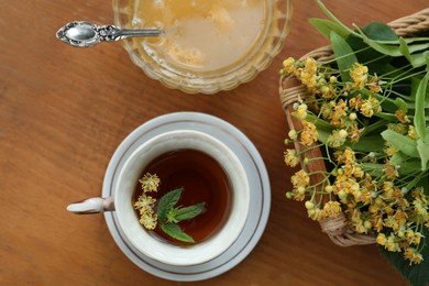 Photo of Cup of hot aromatic herbal tea, honey and linden blossoms on wooden table, flat lay