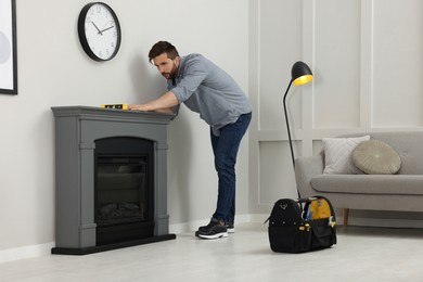 Man using construction level for installing electric fireplace near wall in room
