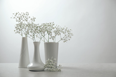 Gypsophila flowers in vases on table against white background. Space for text