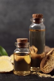 Glass bottles of essential oil, ginger powder and root on dark table