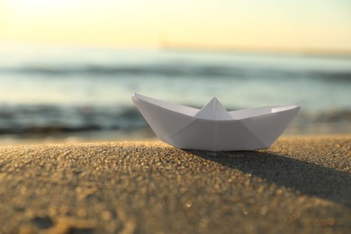 White paper boat on sand near sea at sunset, closeup. Space for text