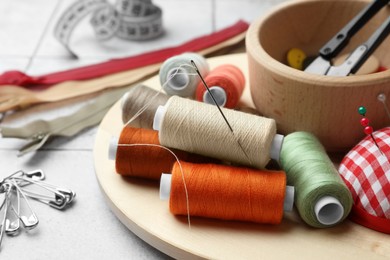 Photo of Spools of threads and sewing tools on light tiles, closeup