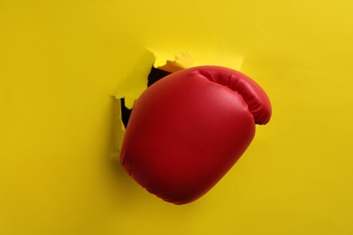 Man breaking through yellow paper with boxing glove, closeup