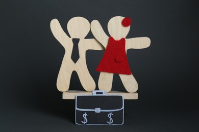 Gender pay gap. Wooden figures of man and woman on miniature seesaw against black background