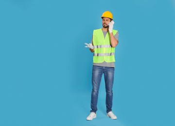 Photo of Male industrial engineer in uniform talking on phone against light blue background