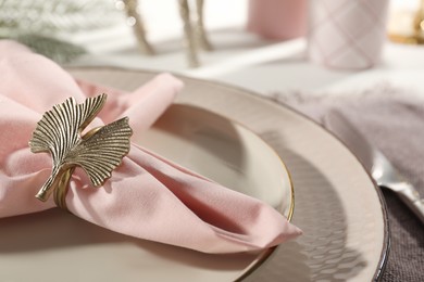 Photo of Pink fabric napkin with beautiful decorative ring for table setting on plate, closeup